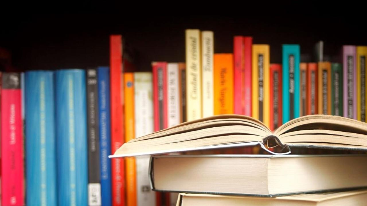 Image of books stacked on top of each other as well as in a shelf